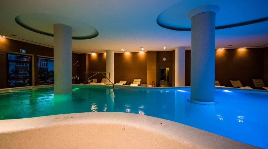 Piscina interna con illuminazione soffusa e sedie a sdraio intorno.